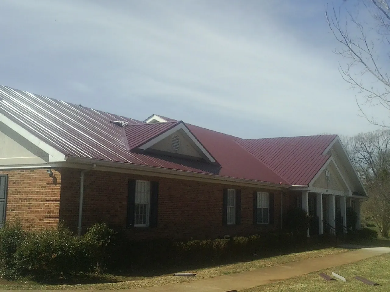 Red metal roof with gabled entries on a long brick building, from a Hail Damage Roof Repair job in Stony Creek