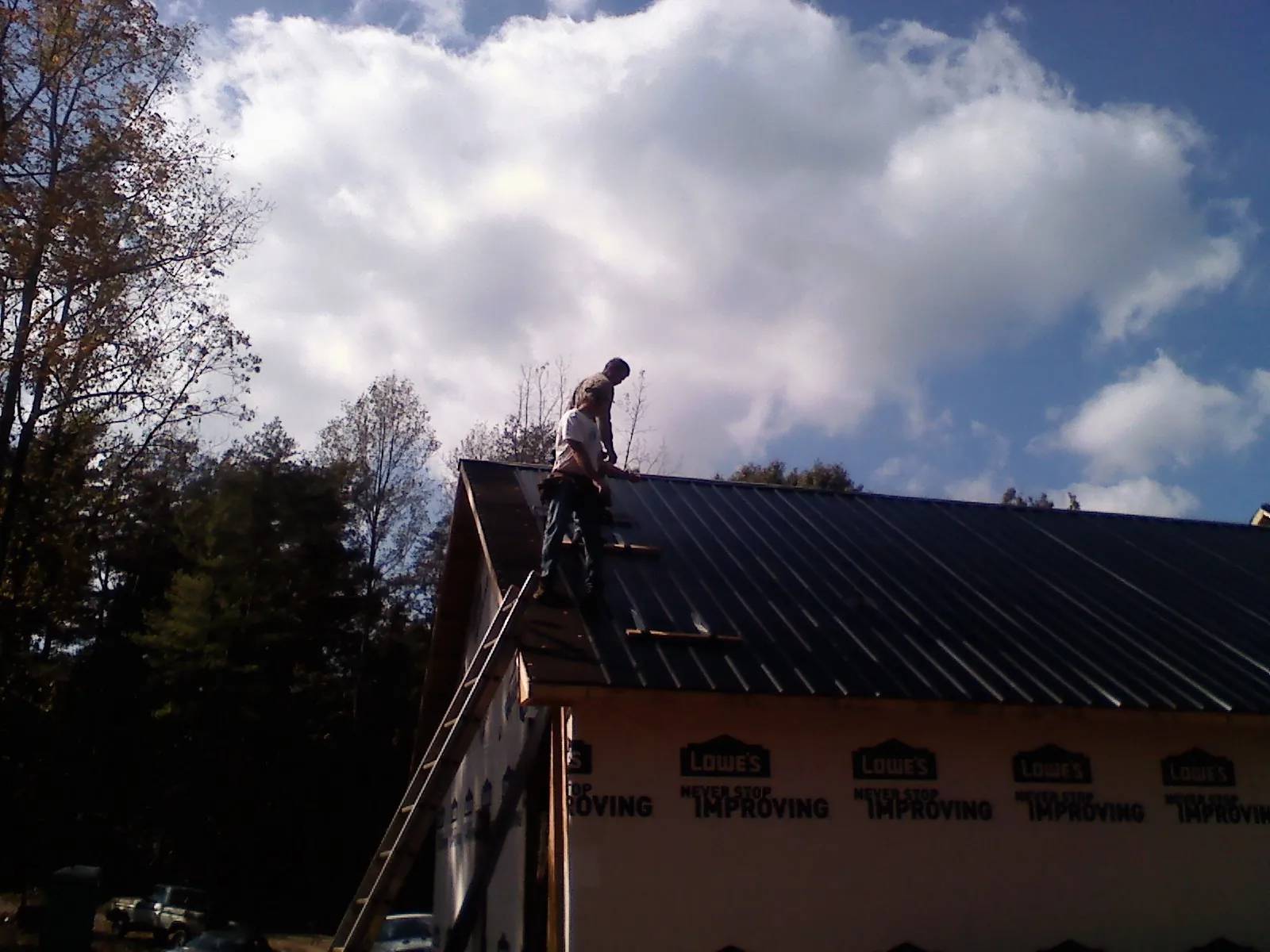 Roofer fastening dark metal panels high against a cloudy sky, from a Roof Inspection job in Stony Creek