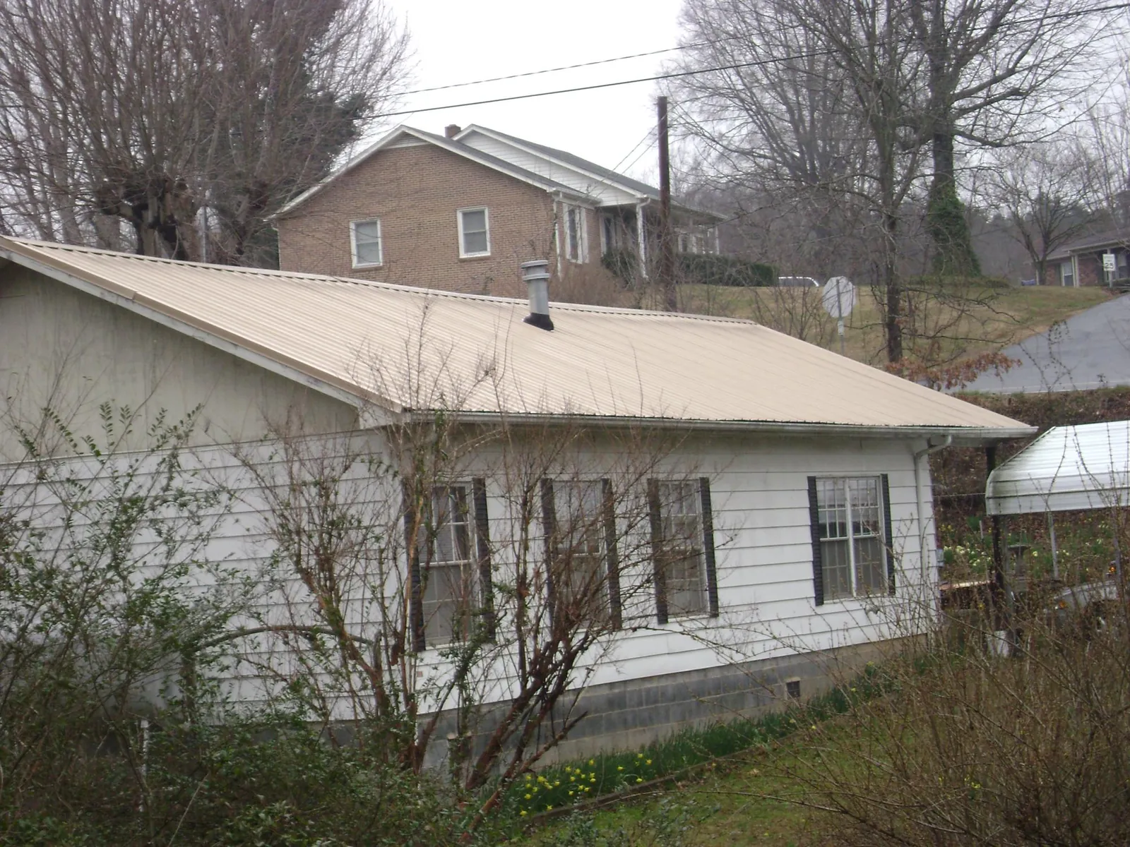 Tan metal roof on a white sided house set into a hillside — Commercial Roofing by Roofing Brothers in Stony Creek